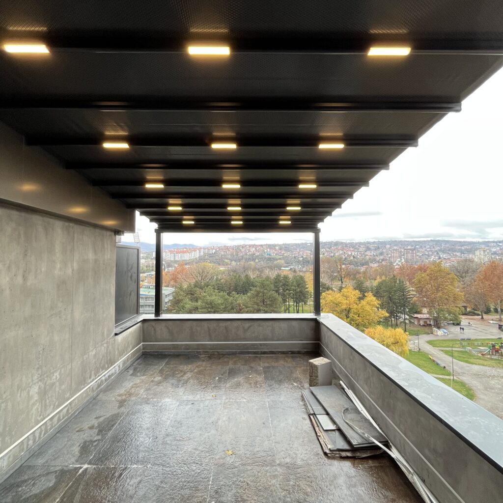 Natkrivena terasa s rasvjetom i prostorom za sjedenje, uređena kao ugodan vanjski dnevni boravak s pogledom na prirodu.