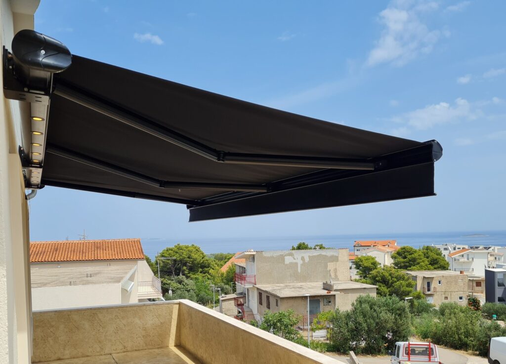 Tenda za terasu u izvučenom položaju koja pruža hlad i zaštitu od sunca, s pogledom na okolinu i naselje.