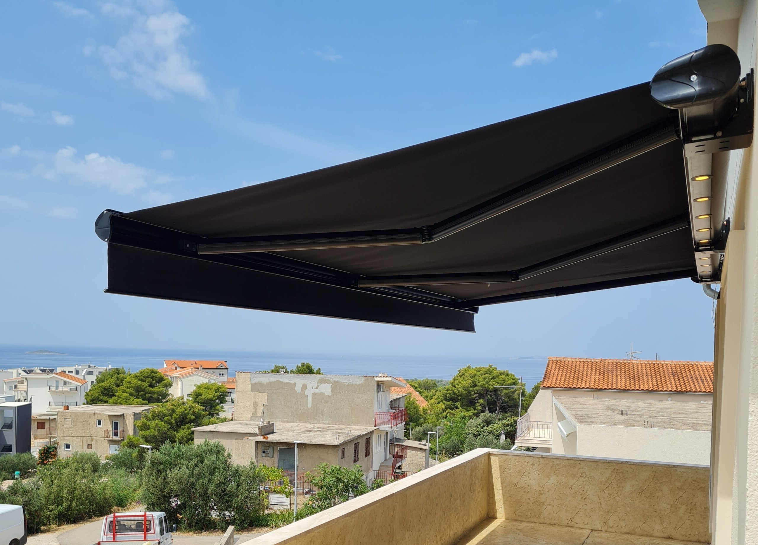 Tenda za terasu u izvučenom položaju koja pruža hlad i zaštitu od sunca, s pogledom na okolinu i naselje.
